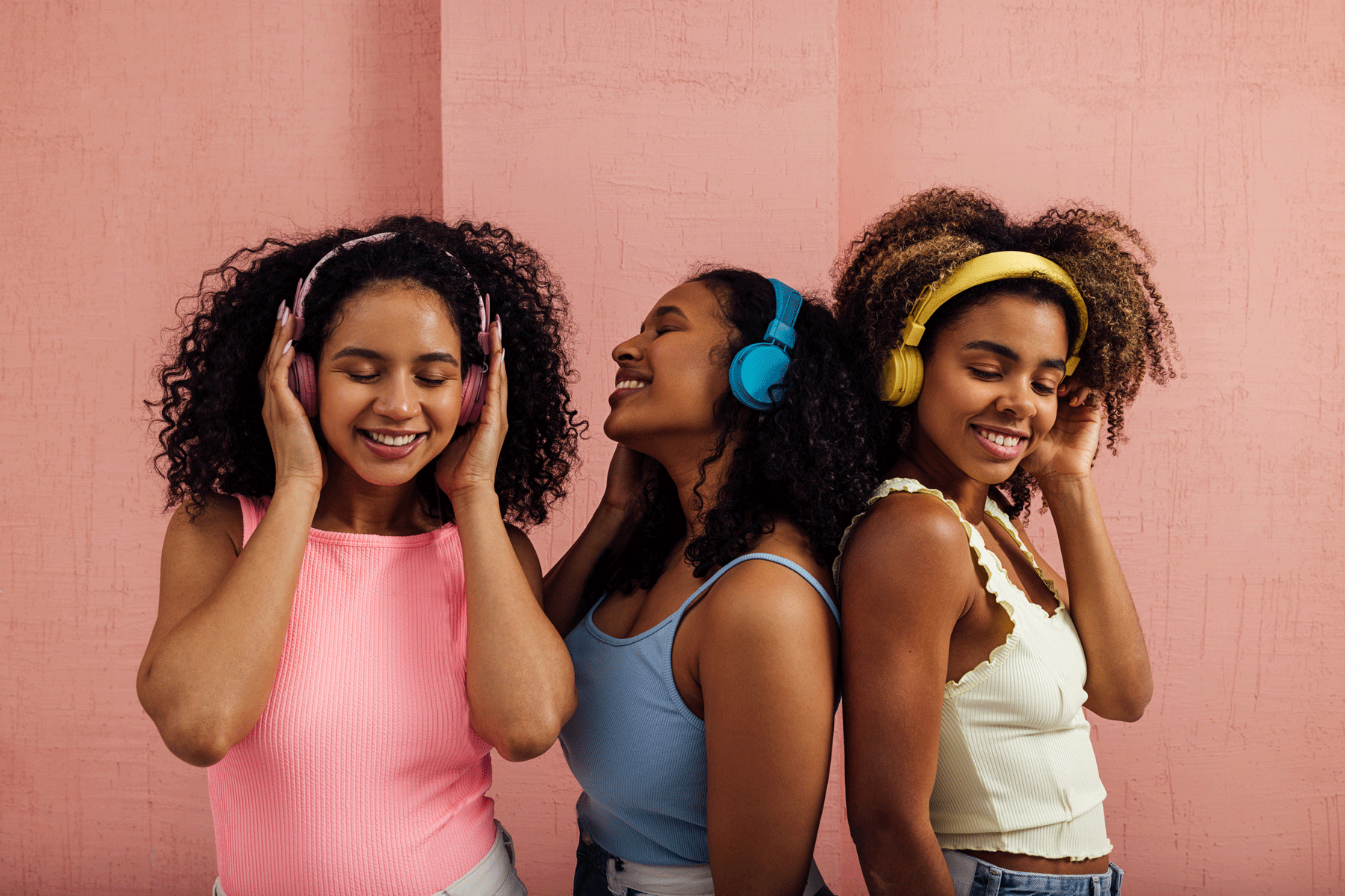 Three women listening to music on headphones which are using Auracast, the latest development in bluetooth audio