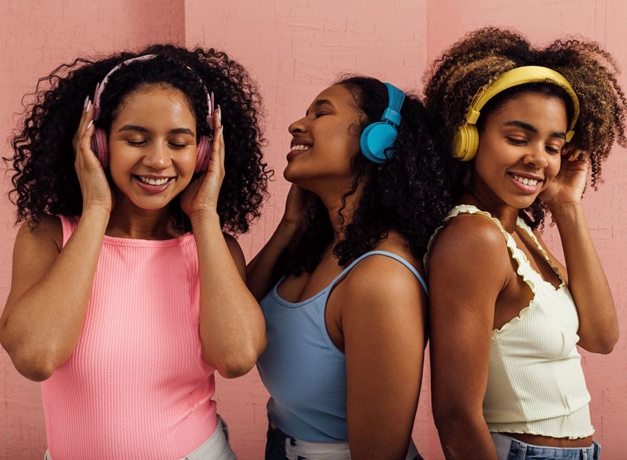 Three women listening to music on headphones which are using Auracast, the latest development in bluetooth audio
